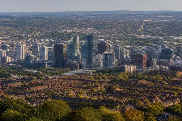 Aerial view from a city centre with tall office towers out to low-rise suburban houses and gardens in late afternoon light